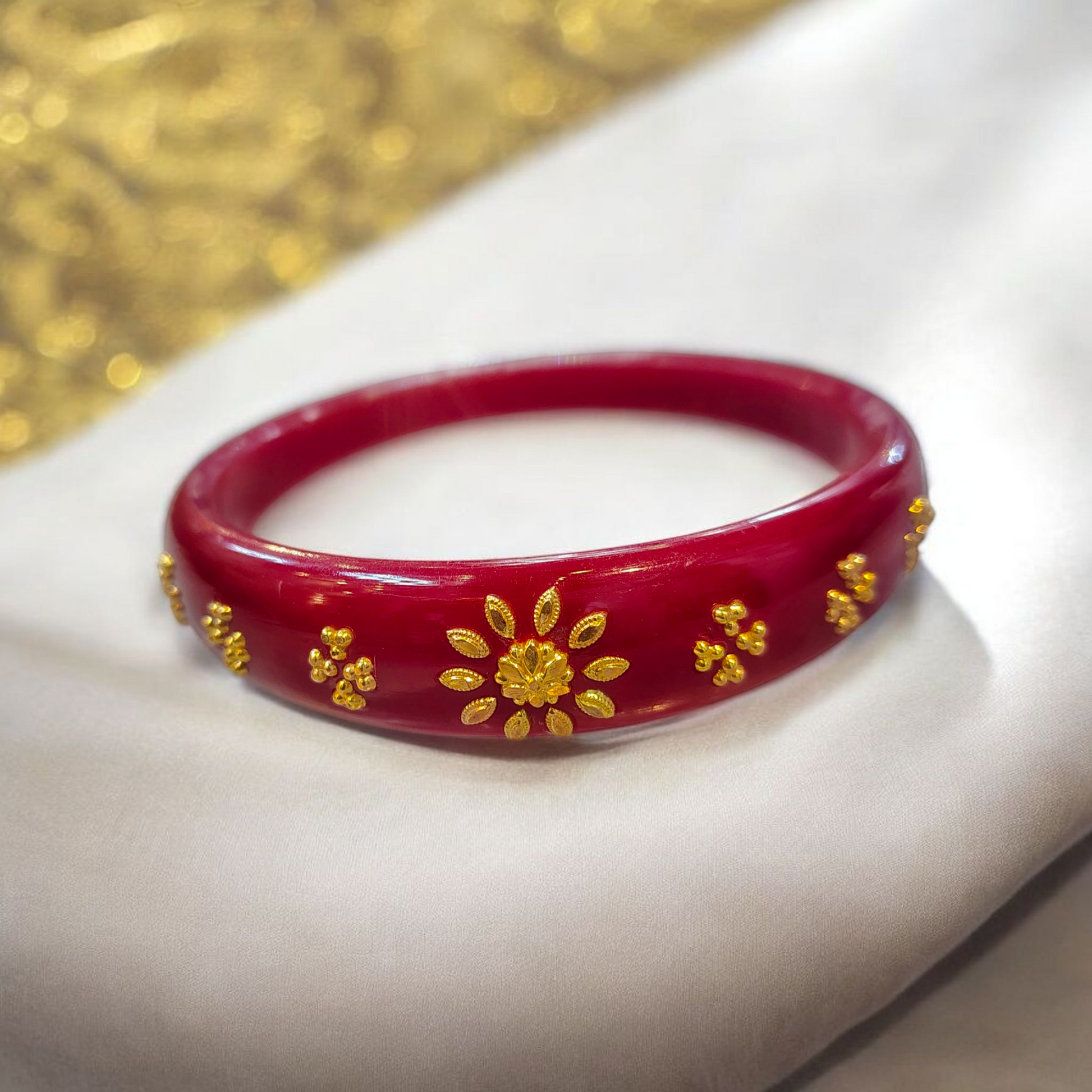 Red bracelet with gold floral designs on a white surface with a gold glittery background